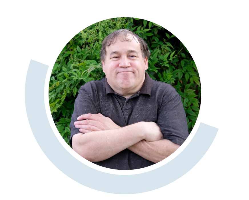 Website header graphic with curved light blue accents, featuring a circular outdoor portrait of a smiling man in a black polo shirt with his arms folded across his chest and green foliage behind him.