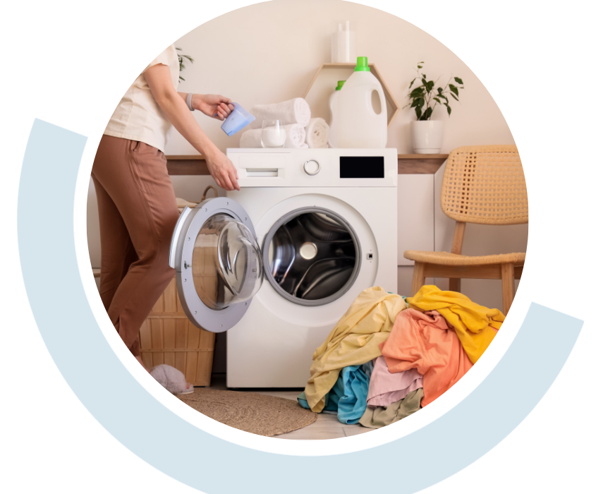 Website header graphic with a pale background and curved light blue accents, featuring a circular photo of a person loading clothes into a front-loading washing machine, representing practical support with everyday household activities.