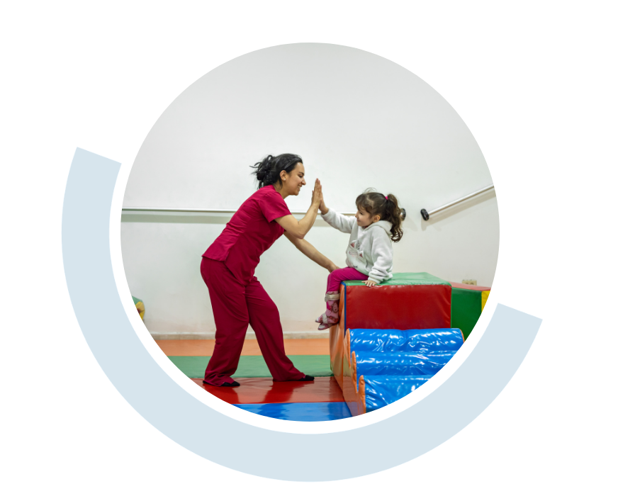 Website header graphic with curved light blue accents, featuring a circular photo of a therapist in red scrubs working with a young child in a therapy room. The child sits on colourful padded equipment while giving a hight five to the therapist.