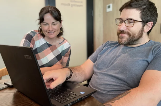 Two people sitting in front of a laptop, looking at the screen together,