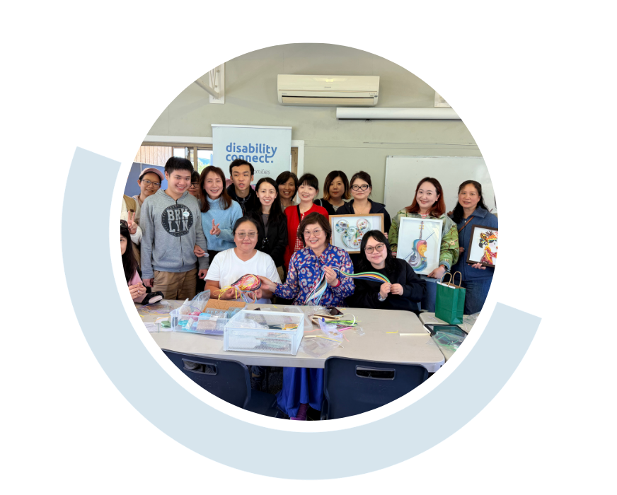 Website header graphic with a pale background and curved light blue accents, featuring a circular group photo of Disability Connect community members gathered together indoors and smiling at the camera, showing their craft creations.