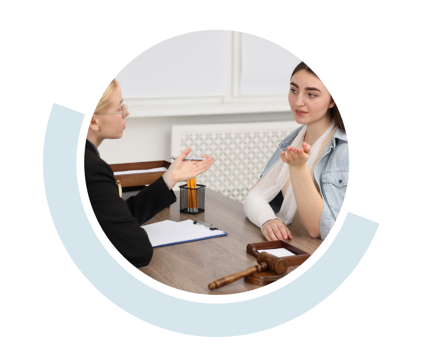 Website header graphic with a pale background and curved light blue accents, featuring a circular photo of two women discussing a legal matter across a desk. Papers and a judge’s gavel sit on the table between them.