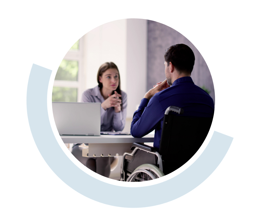 Website header graphic with a pale background and curved light blue accents, featuring a circular photo of a woman speaking with a wheelchair user across a desk in a professional office setting.