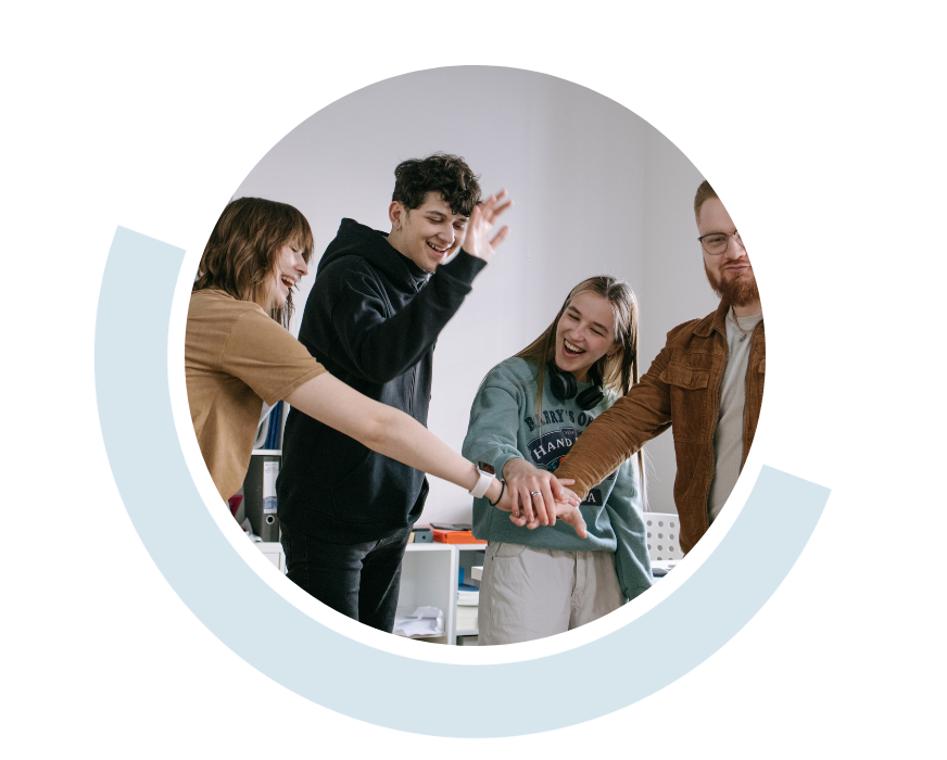 Website header graphic with a pale background and curved light blue accents, featuring a circular photo of four people smiling and stacking their hands together in the centre during a supportive group activity.
